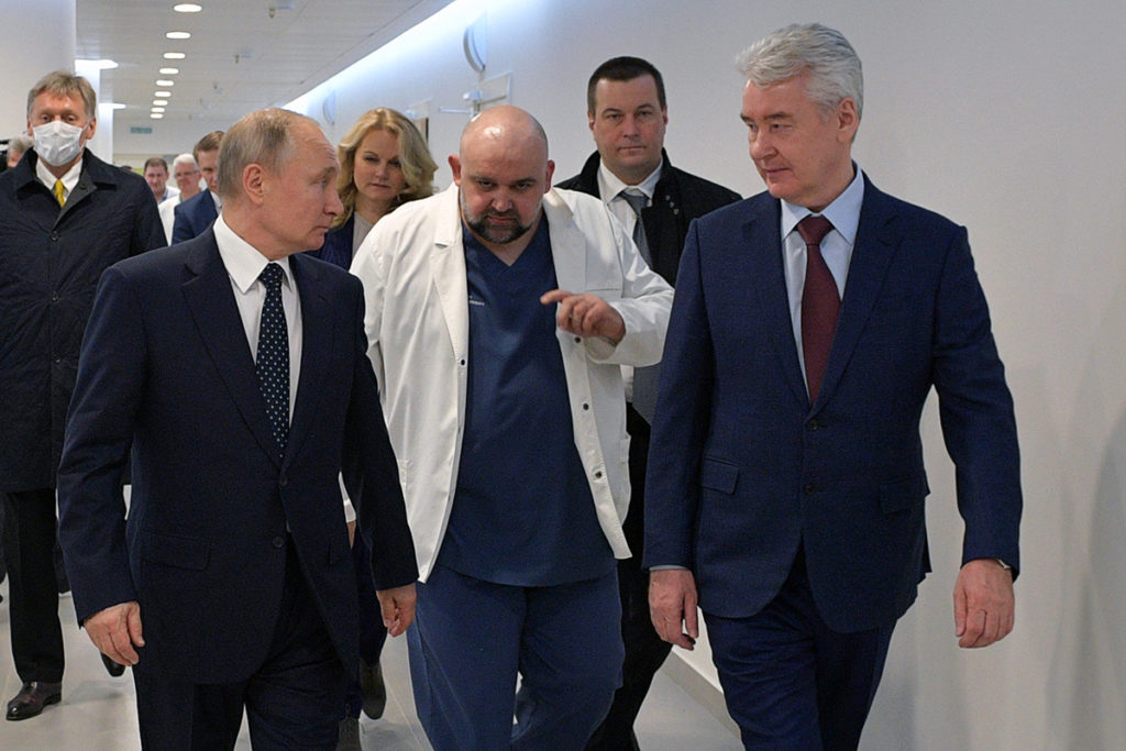 Дмитрий Песков (на заднем плане слева) во время визита Владимира Путина в больницу в Коммунарке