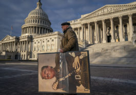 Анти-Трамповский активист с портретом Трампа на фоне здания Конгресса США в Вашингтоне