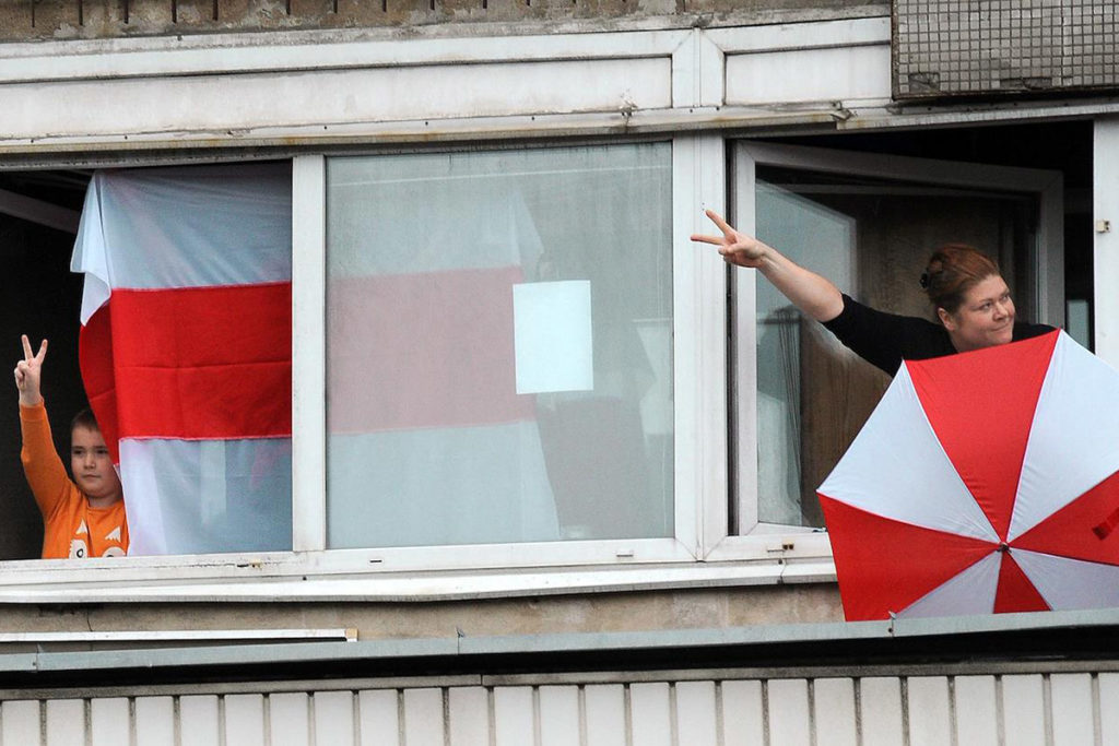 Жители Минска с бело-красно-белым флагом и зонтом поддерживают с балкона участников акции