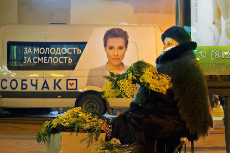 Продавщица цветов на фоне рекламы на микроавтобусе штаба кандидата в президенты Ксении Собчак накануне праздника 8 марта