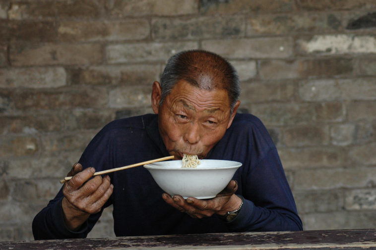 Пожилой мужчина ест лапшу. Пекин, Китай