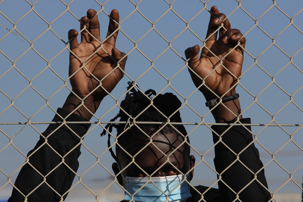 Мигрант в маске стоит за забором в лагере для беженцев на Кипре