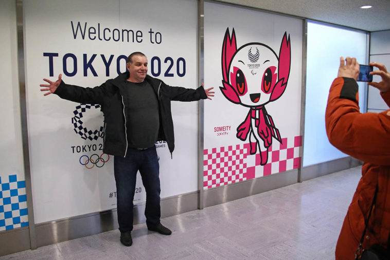 Мужчина фотографируется на фоне рекламы летних Олимпийских игр 2020 года и талисмана Паралимпиады "Сомейти"